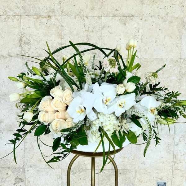 White roses and orchids arranged in a low centerpiece on a stand
