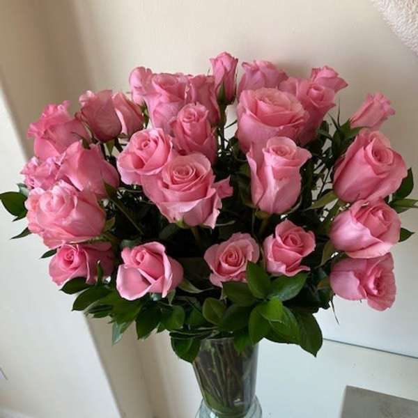 Tall arrangement of pink roses in a clear glass vase on a glass table