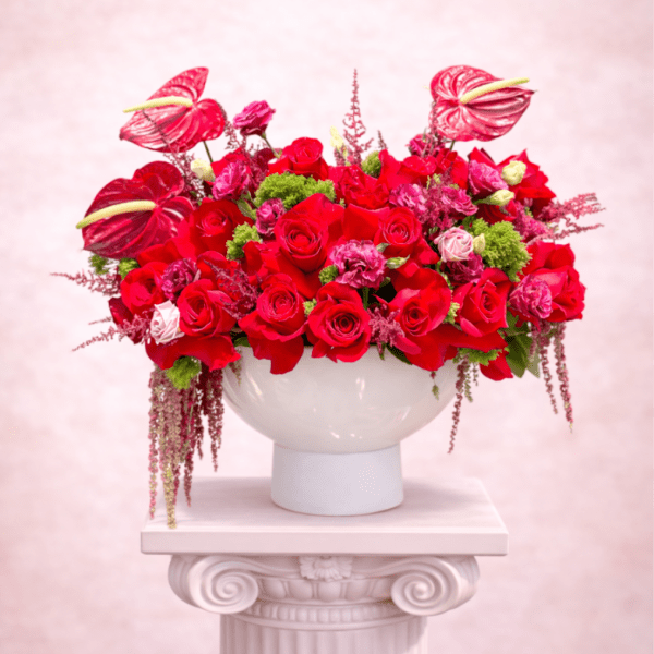 Red rose arrangement in a white pedestal vase with pink anthuriums