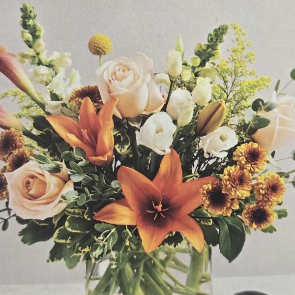 Bouquet of orange lilies, peach roses, and white blooms in a glass vase
