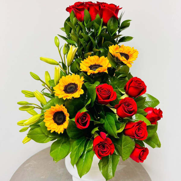 Red roses and yellow sunflowers arranged in a white vase