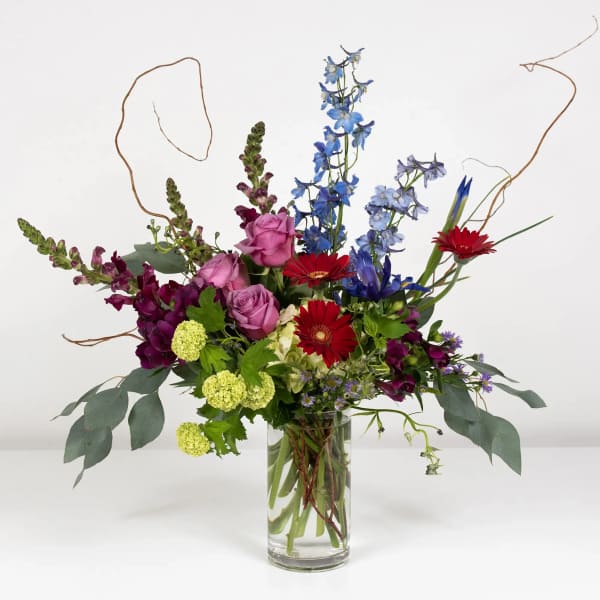 Mixed bouquet in a clear glass vase with red, purple, and blue flowers