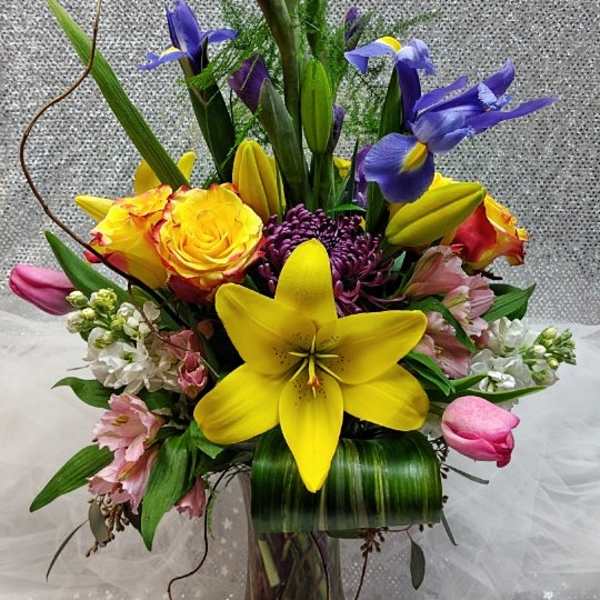 Tall mixed bouquet in a glass vase with yellow lilies and purple irises