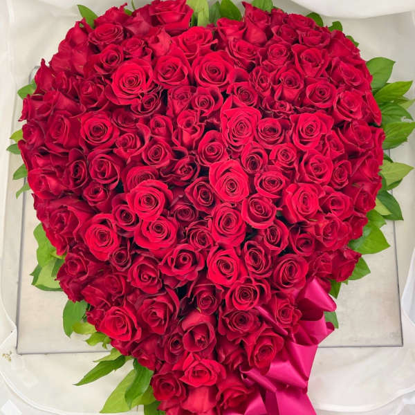 Heart-shaped bouquet of red roses with a pink ribbon