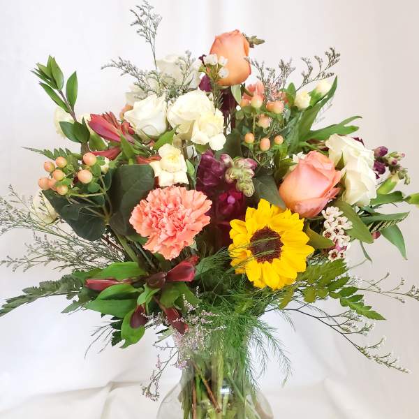 Mixed bouquet of roses, sunflower, and carnations in a glass vase