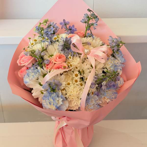 Bouquet of pink roses, white daisies, and blue flowers wrapped in pink paper