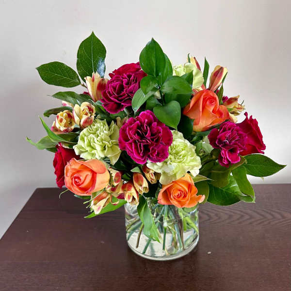 Mixed bouquet of roses, carnations, and alstroemeria in a clear glass vase