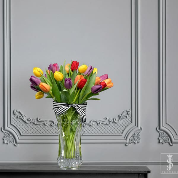 Bouquet of multicolored tulips in a clear glass vase with a striped ribbon