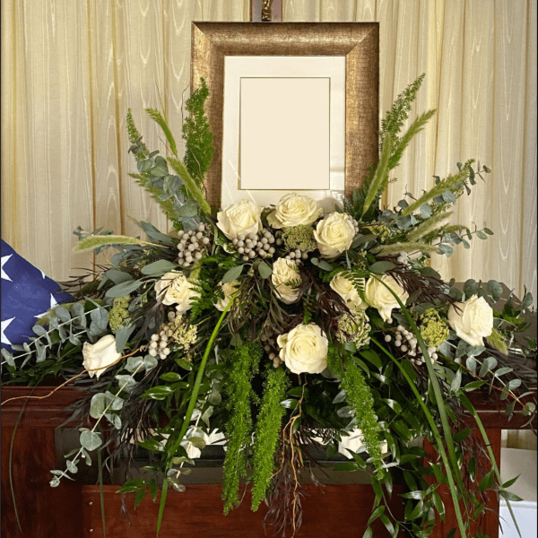 Large white rose arrangement with mixed greenery in front of a framed display