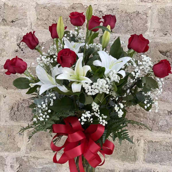 Red roses and white lilies in a glass vase with a red ribbon