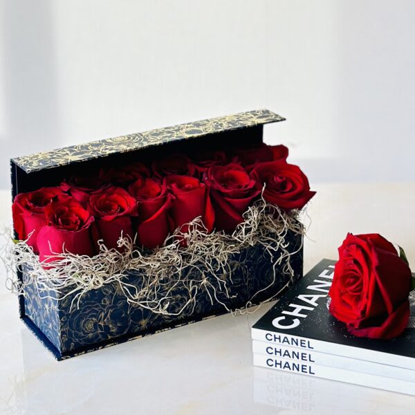 Red roses in a decorative gift box beside a single rose on books