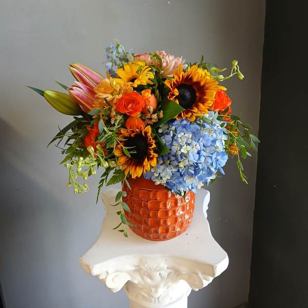 Colorful mixed bouquet in an orange textured vase with sunflowers and blue hydrangea