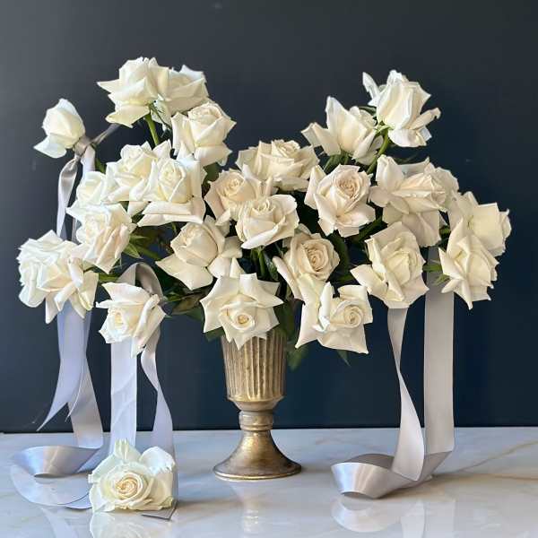 White roses arranged in a gold vase with long satin ribbons.