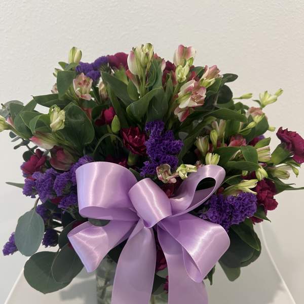 Bouquet of pink and purple flowers with a lavender ribbon in a glass vase