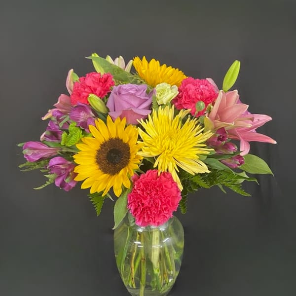 Mixed bouquet of sunflowers, lilies, roses, and carnations in a glass vase