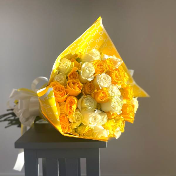 Bouquet of yellow and white roses wrapped in bright yellow paper