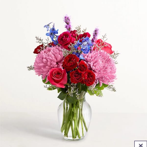 Bouquet of pink, red, and blue flowers in a clear glass vase