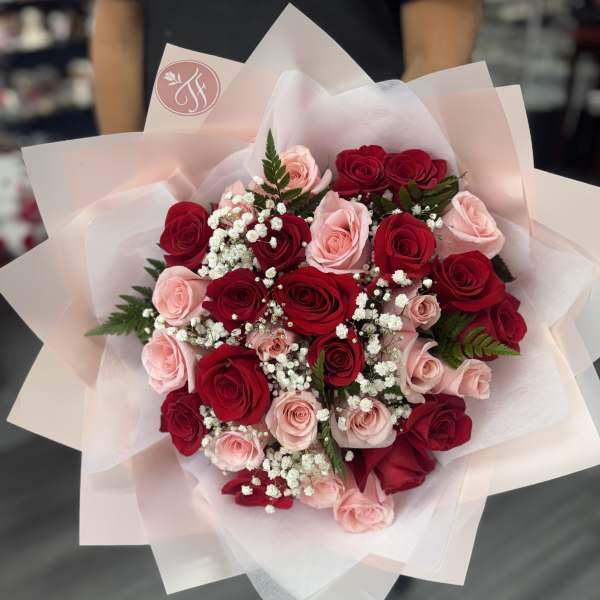 Bouquet of red and blush roses with white baby's breath in pale pink wrap