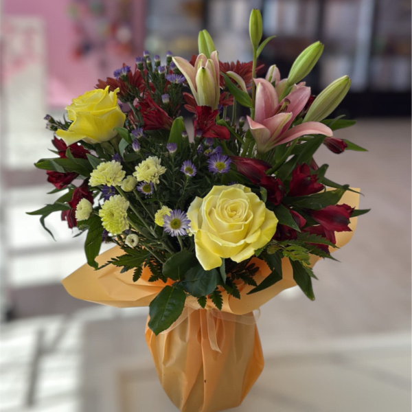 Bouquet of yellow roses, pink lilies, and red flowers wrapped in peach paper