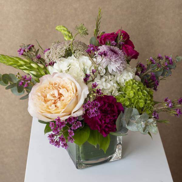 Mixed bouquet in a square glass vase with peach, white, and magenta blooms