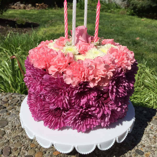 Pink and purple flower-covered cake with four striped candles