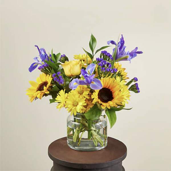 Yellow sunflowers and purple flowers in a clear glass vase