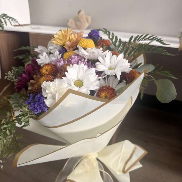 Bouquet of mixed daisies and chrysanthemums wrapped in cream paper