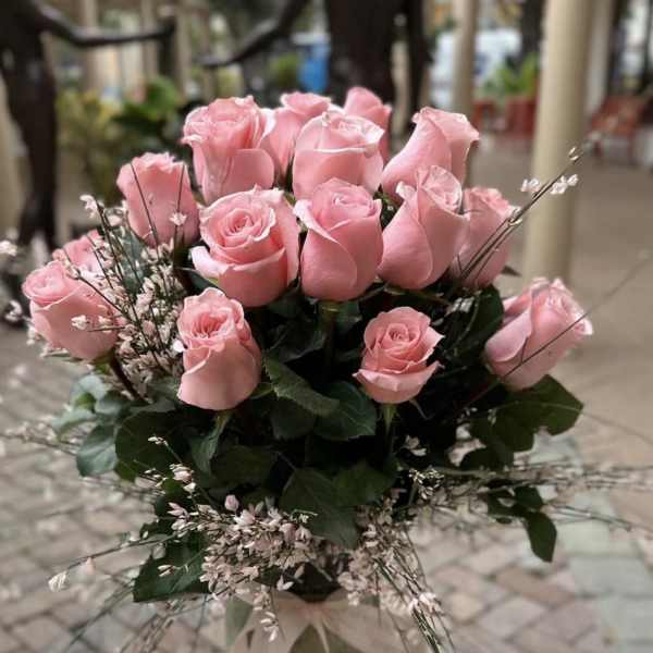 Tall arrangement of pink roses with delicate filler flowers in a glass vase tied with a ribbon