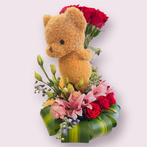Teddy bear with red roses and pink lilies in a leaf-wrapped base