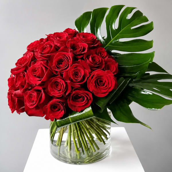 Bouquet of red roses in a clear glass vase with large tropical leaves