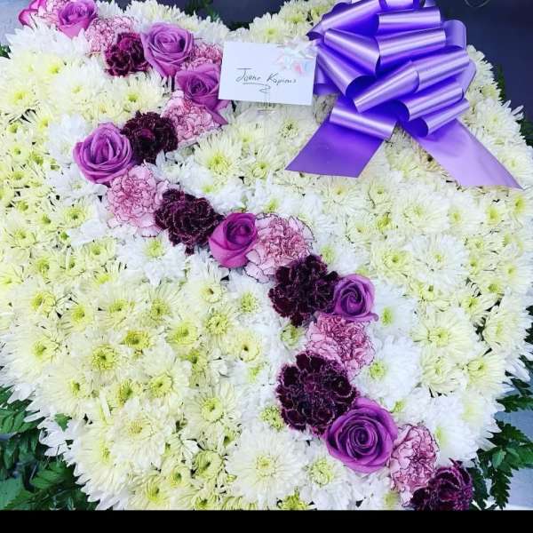 Heart-shaped floral tribute with purple roses and a ribbon bow