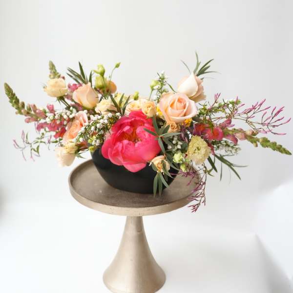 Mixed bouquet of peach and pink flowers in a black bowl on a pedestal stand