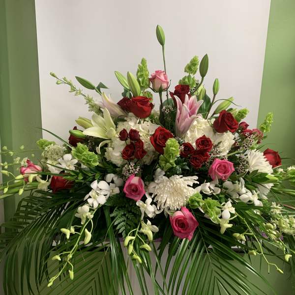 Large floral arrangement with red, pink, and white blooms in a low container