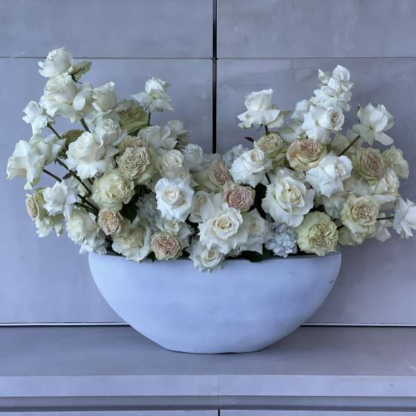 White roses and cream flowers arranged in a white bowl vase