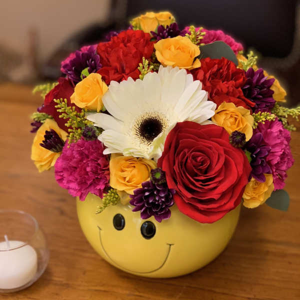 Colorful mixed flower arrangement in a yellow smiley-face container