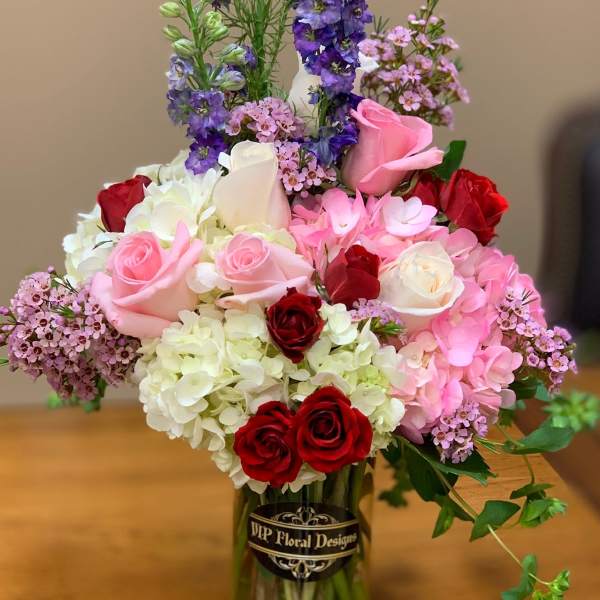Mixed bouquet of roses, hydrangeas, and purple flowers in a glass vase