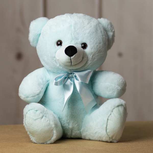 Light blue teddy bear with a satin bow sitting on a table