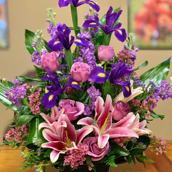 Pink roses and lilies arranged with purple irises in a black vase