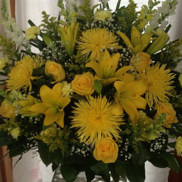 Yellow lilies and roses arranged with white snapdragons in a large display.