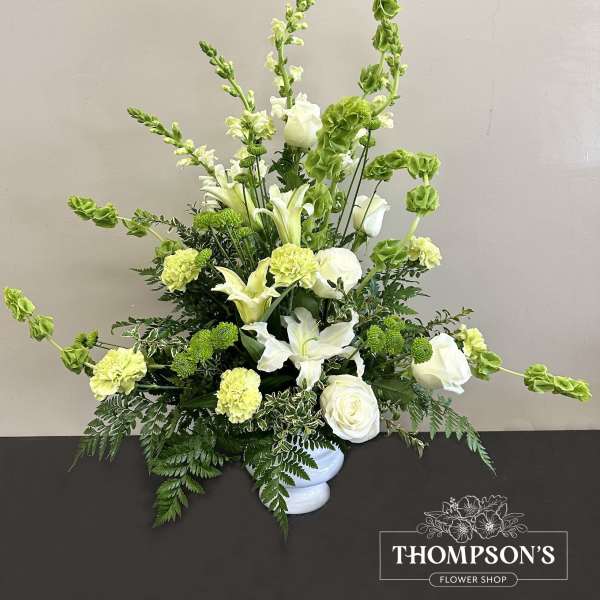 Tall white and green arrangement with lilies, roses, carnations, and Bells of Ireland in a white vase