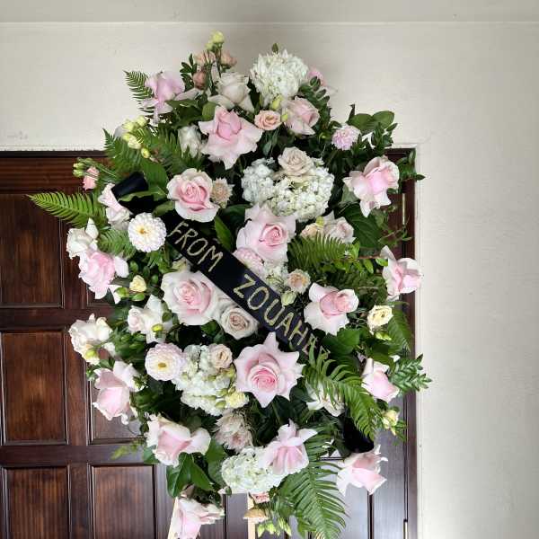 Large pink and white funeral wreath on an easel with a black ribbon