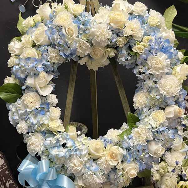 Heart-shaped floral wreath with white roses and blue hydrangeas on an easel