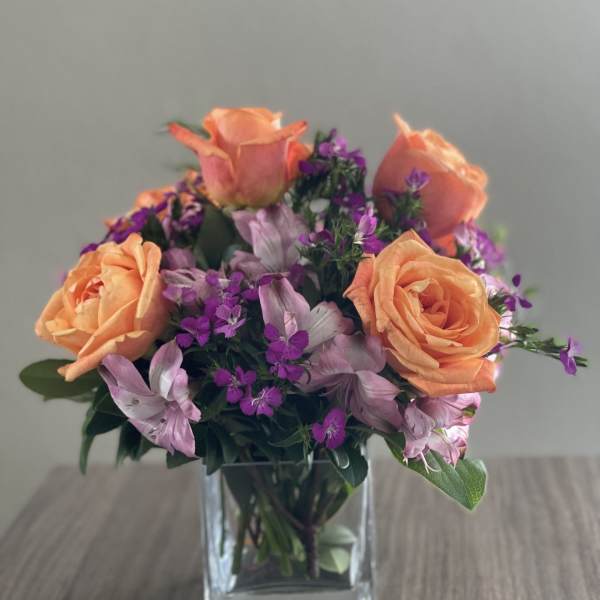 Peach roses and purple flowers in a clear glass vase