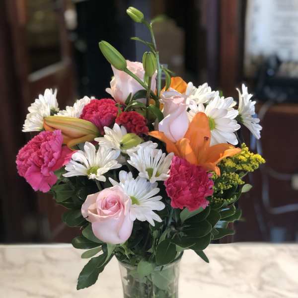Mixed bouquet of pink roses, lilies, carnations, and white daisies in a glass vase