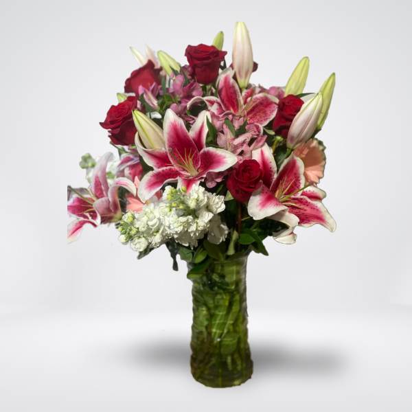 Bouquet of red roses and pink lilies in a green glass vase