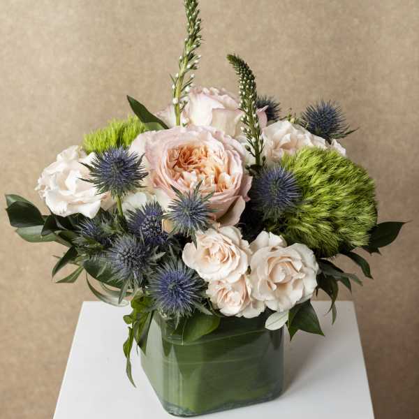 Peach and white roses in a green glass vase with blue thistle and green pom-pom flowers