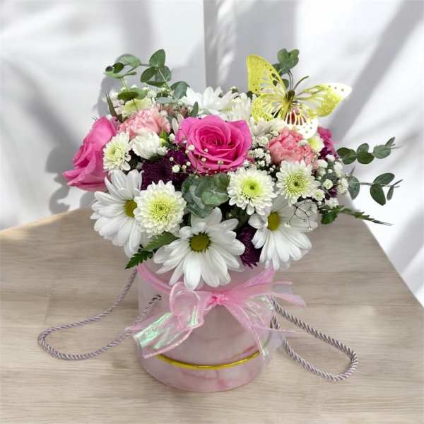 Round pink hatbox arrangement with pink roses, white daisies, and a yellow decorative butterfly.