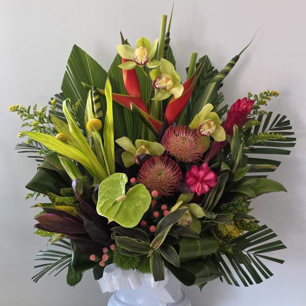 Tropical flower arrangement in a white pedestal vase with pink and green blooms
