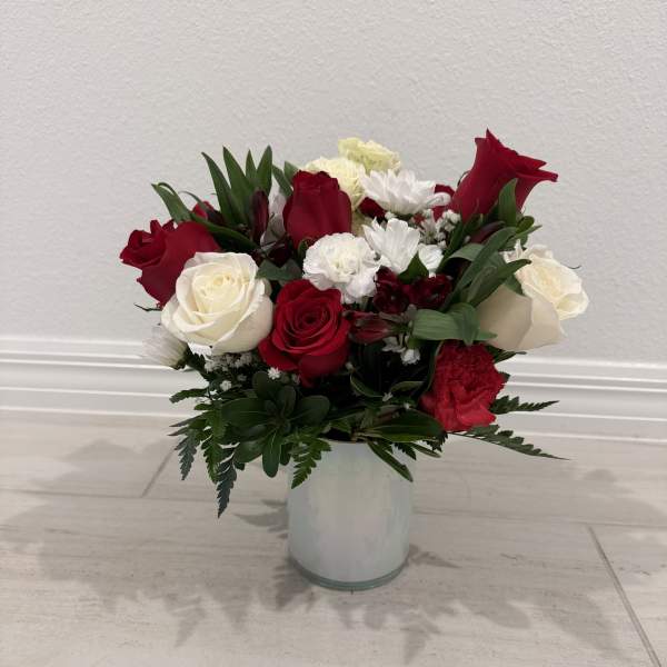 Red and white roses with white daisies in a clear glass vase
