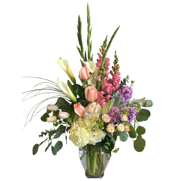 Tall mixed bouquet with peach roses, white calla lilies, and purple flowers in a glass vase